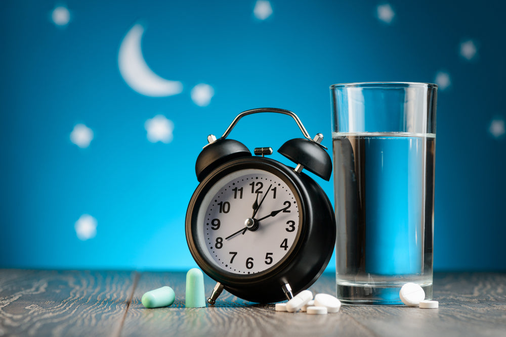 Analog-alarm-clock-with-glass-of-water-pills-and-earplugs-on-wooden-table