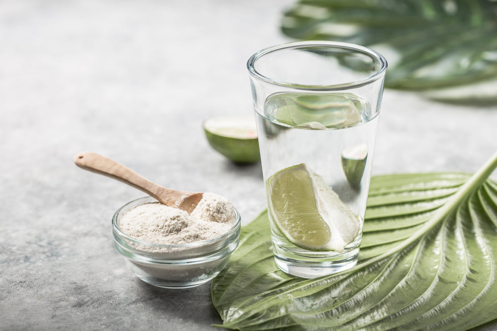 Collagen-powder-in-glass-bowl-with-wooden-spoon-beside-glass-of-water-with-slice-of-lime.