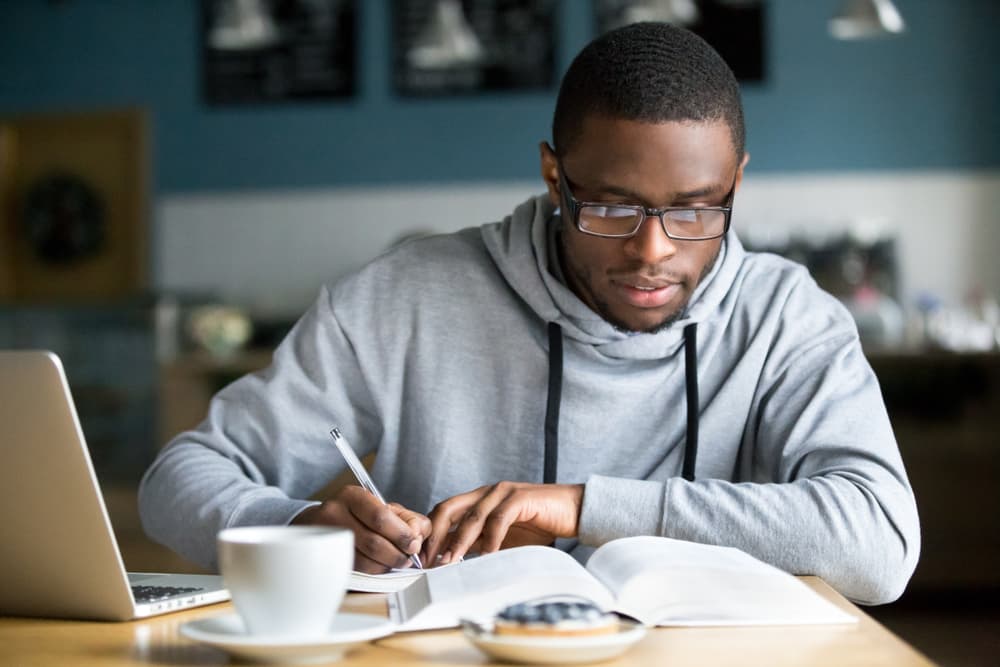 Focused young African American man in glasses reading and taking notes