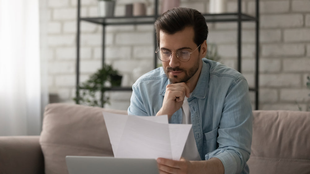 Man-wearing-glasses-concentrating-on-reading-papers-while-sitting-on-sofa