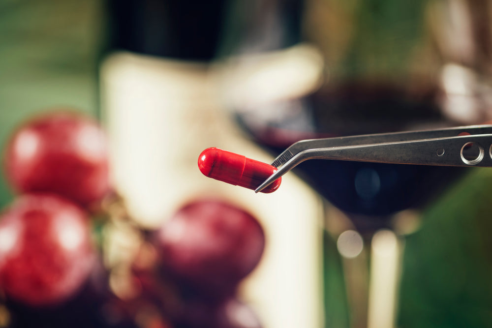 Red-resveratrol-supplement-capsule-with-grapes-and-glass-of-wine-blurred-in-background