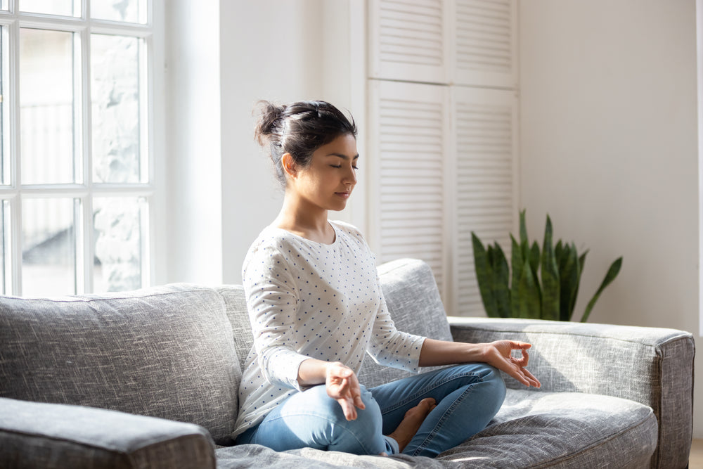 Young-Indian-woman-sitting-on-sofa-in-lotus-yoga-pose.