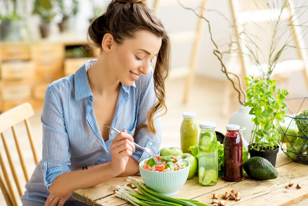 Young woman smiling while eating healthy salad with vegetables