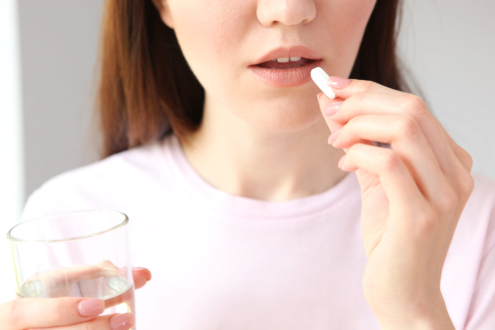 Young-woman-taking-organ-meat-supplement-capsule-with-glass-of-water